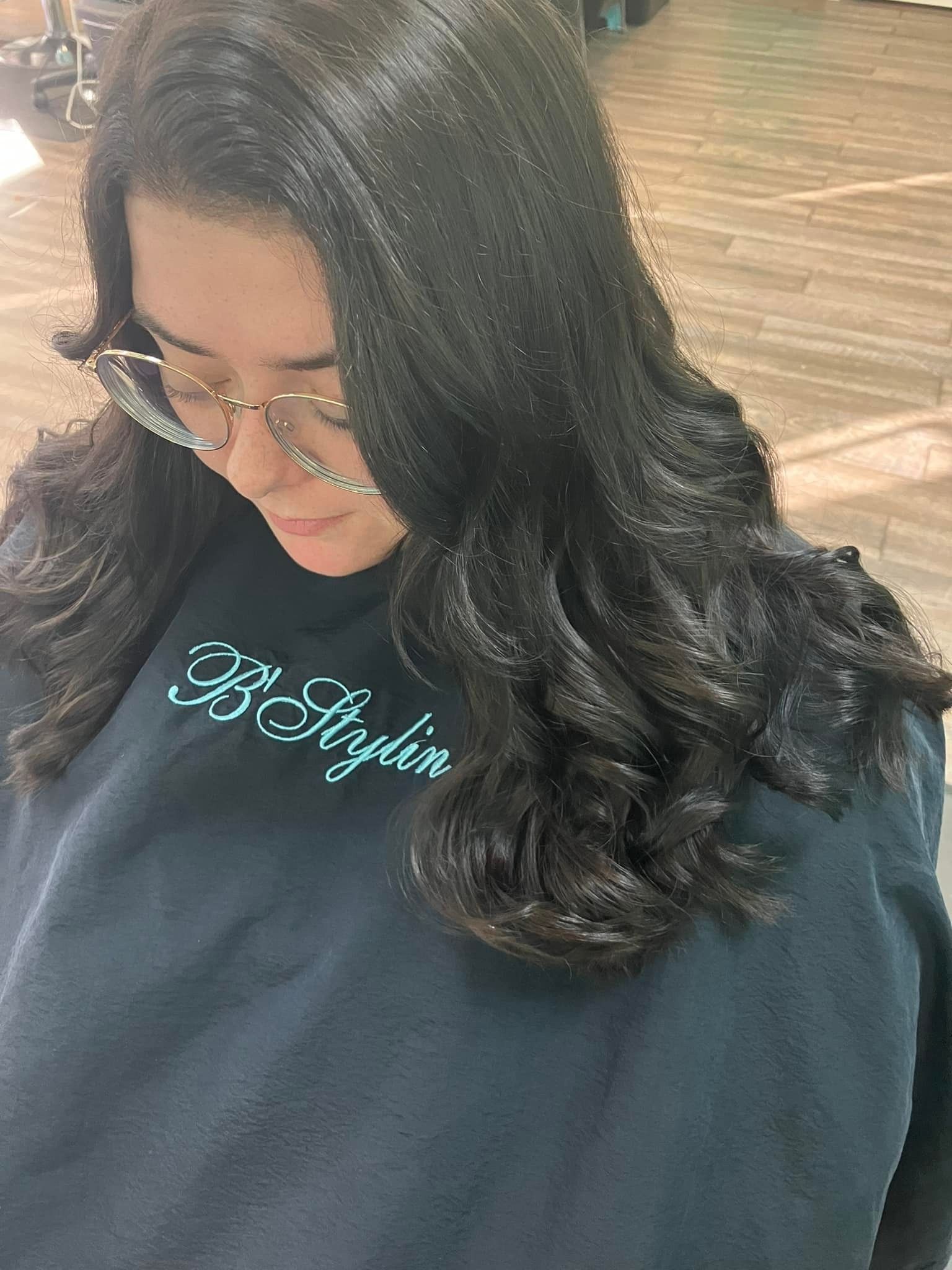 A woman with long black hair is wearing glasses and a cape.