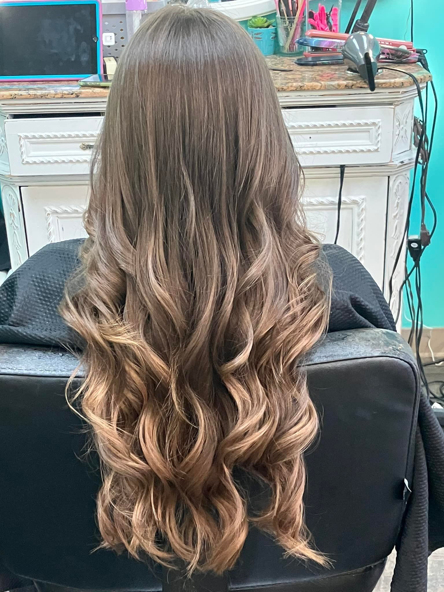 A woman with long wavy hair is sitting in a chair in a salon.