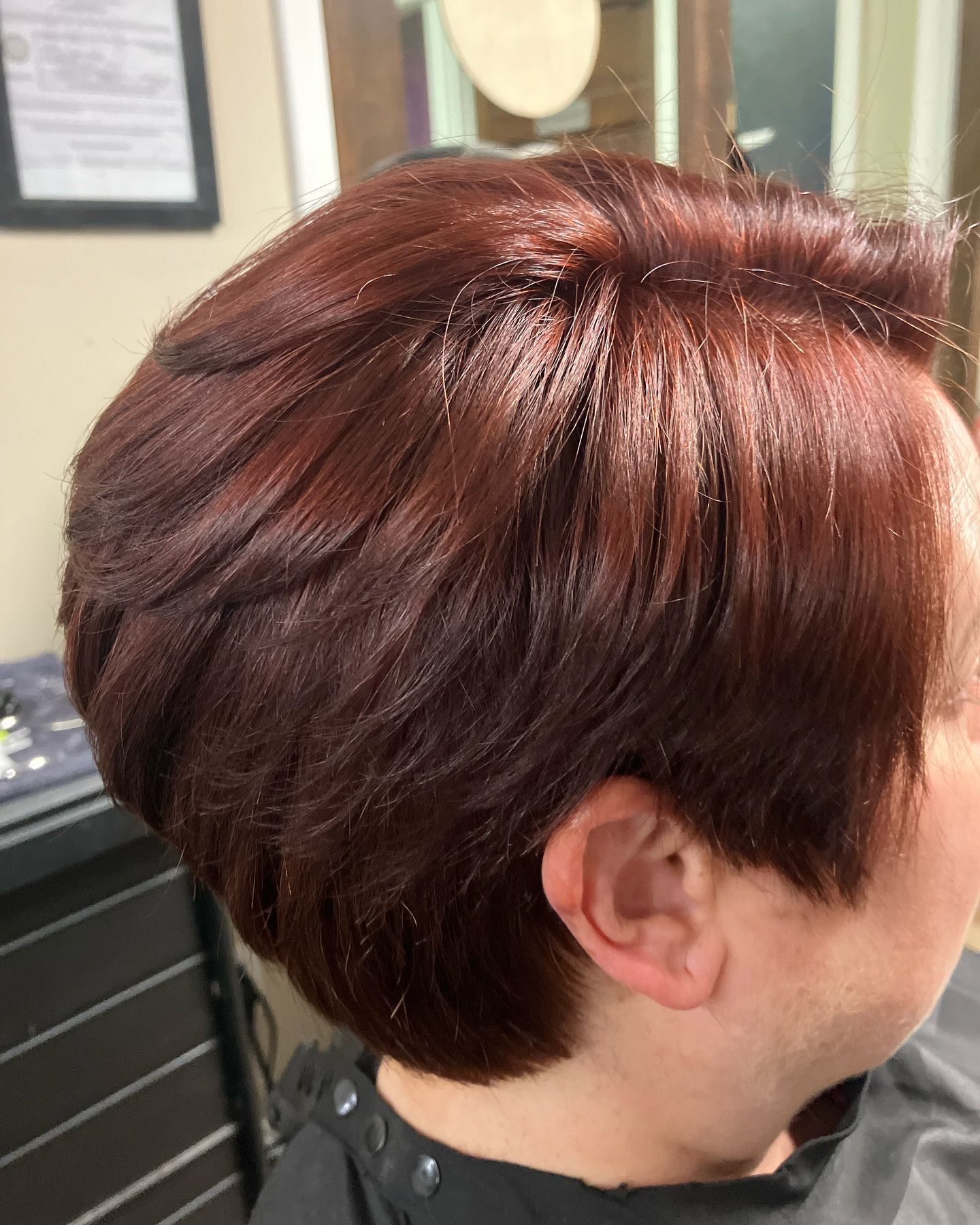 A woman with short red hair is getting her hair cut in a salon.