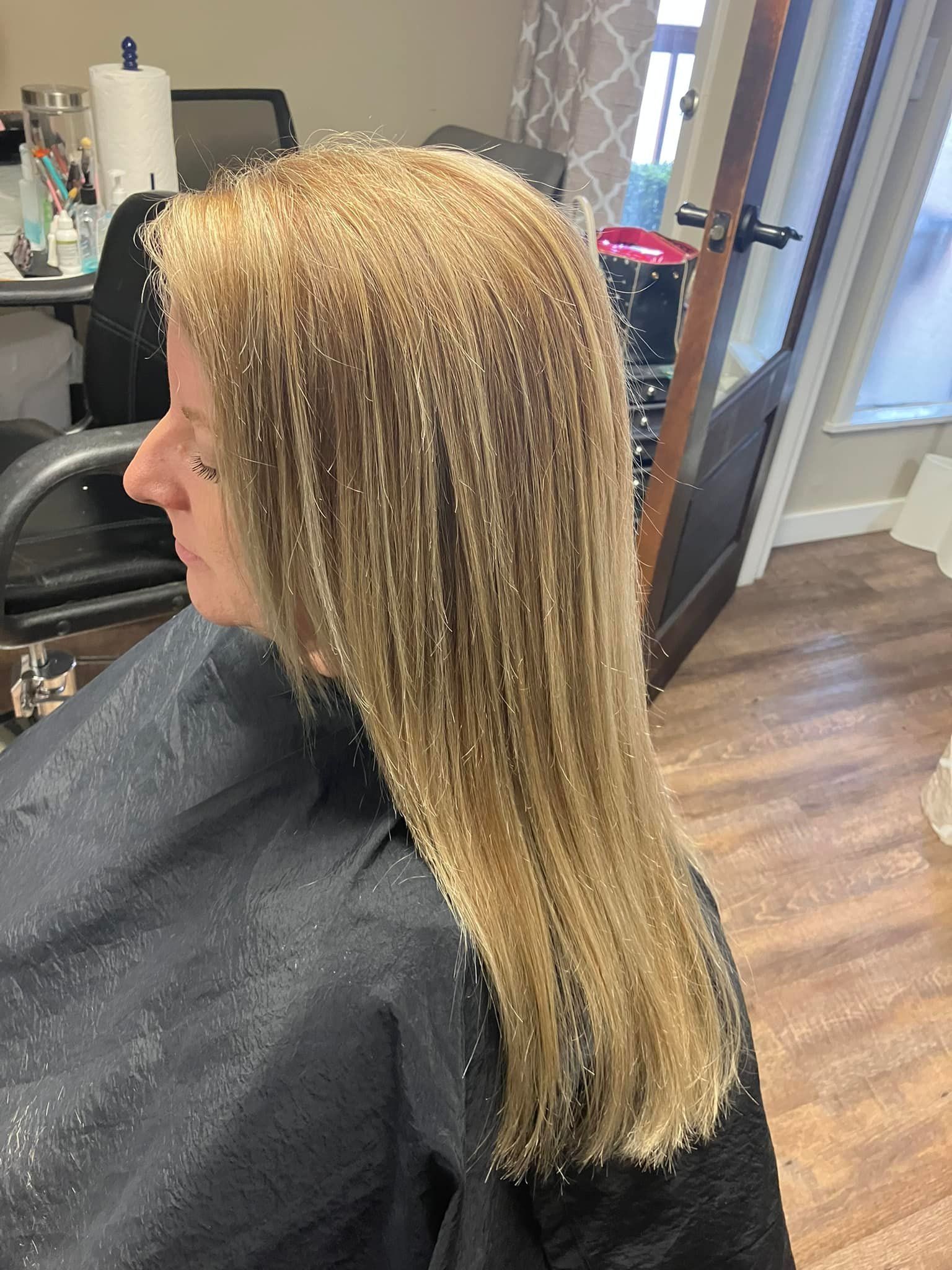 A woman with long blonde hair is sitting in a chair in a salon.