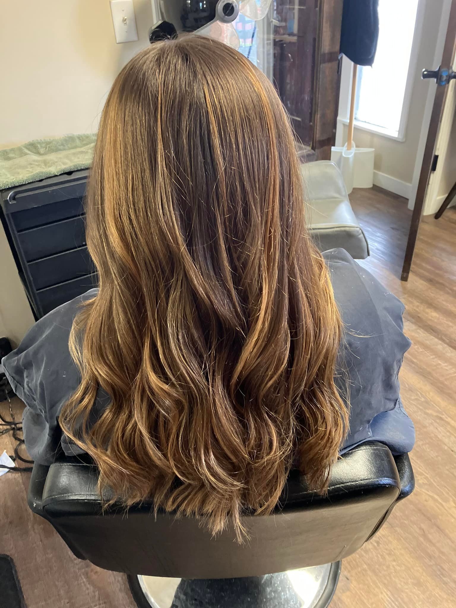 A woman with long brown hair is sitting in a chair in a salon.