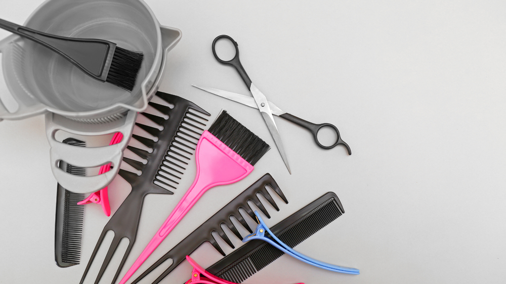 A bunch of hair brushes , scissors , combs and a bowl of hair dye on a table.