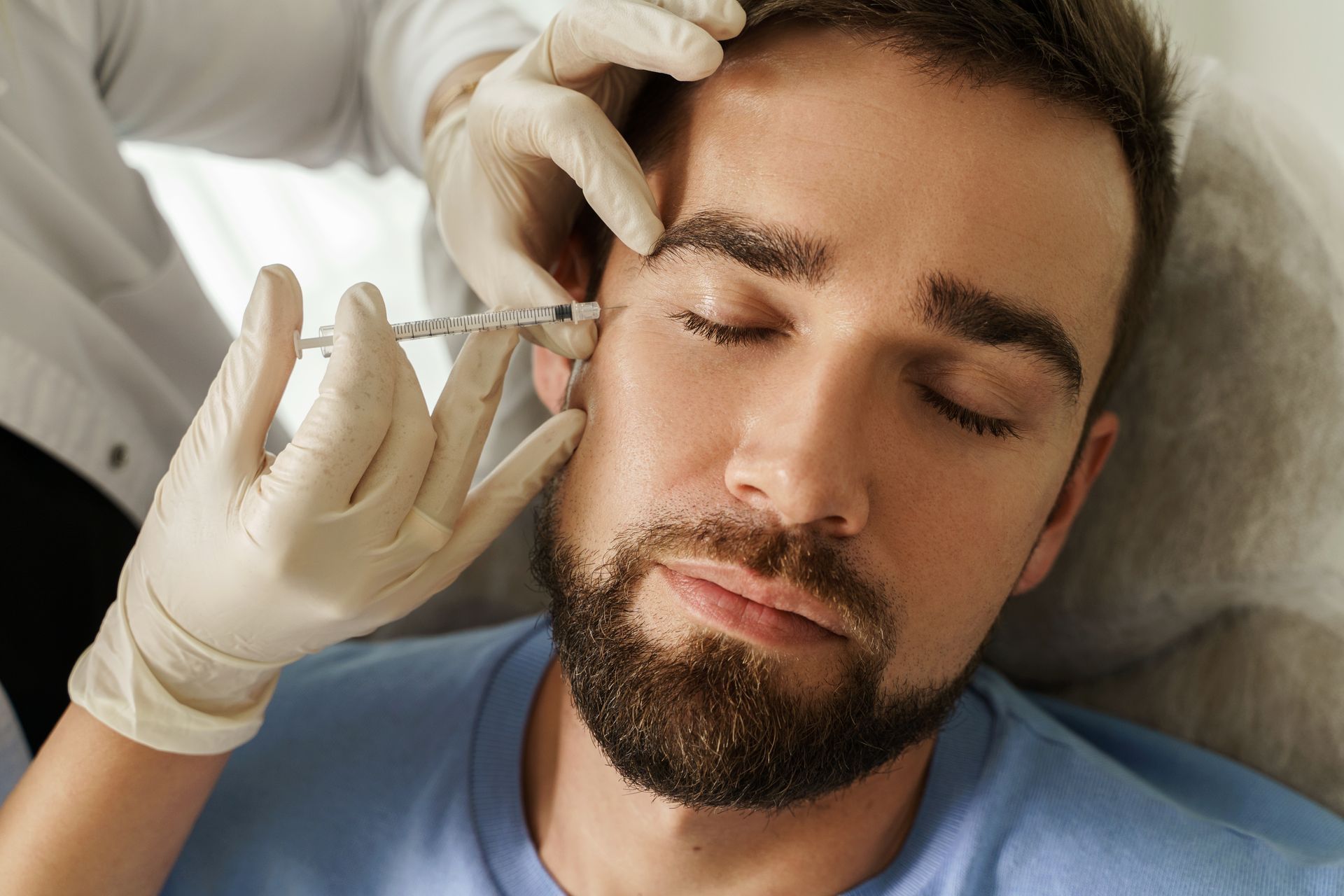 Man receiving injection near eye from gloved hand.
