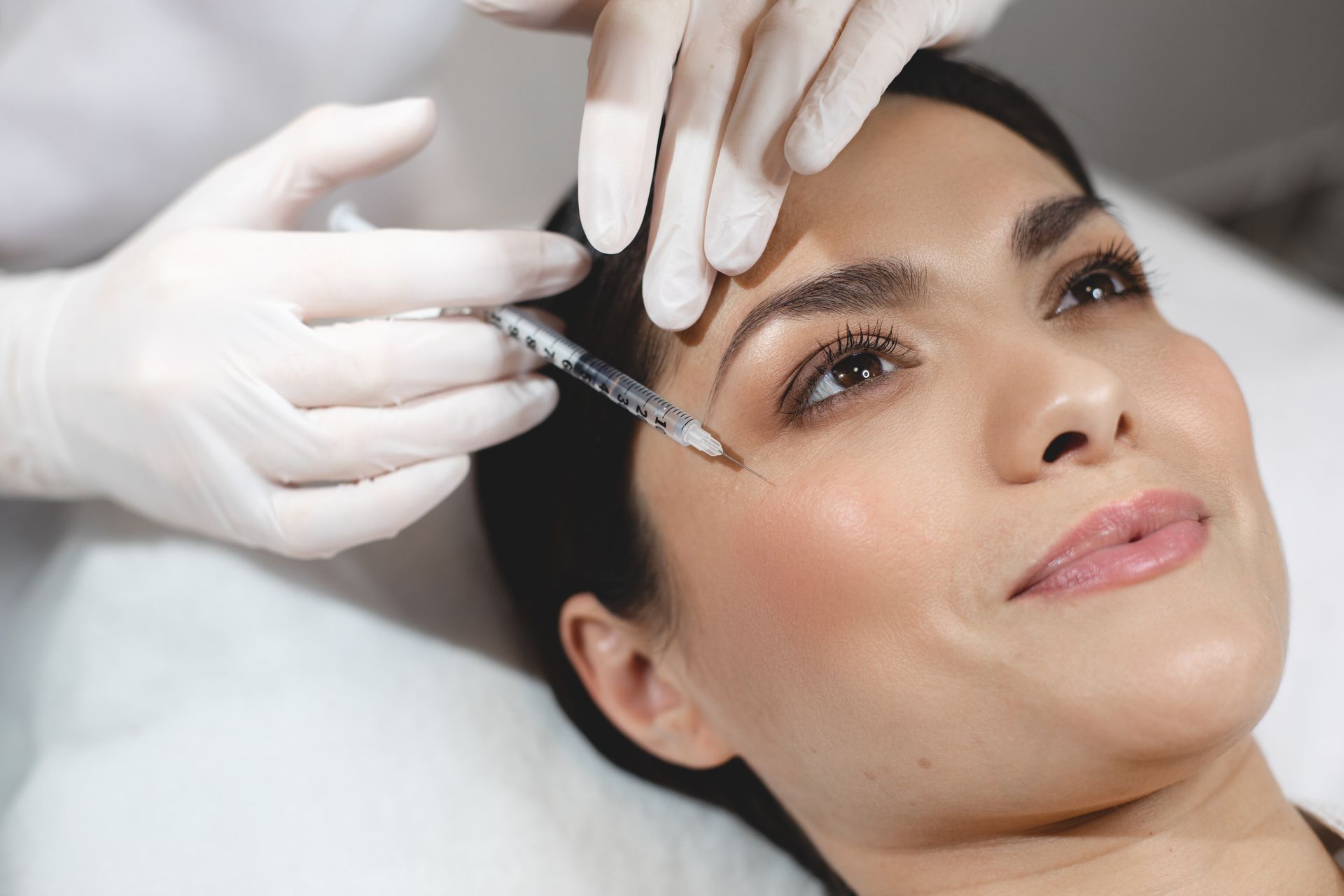 A woman is getting a botox injection in her forehead.