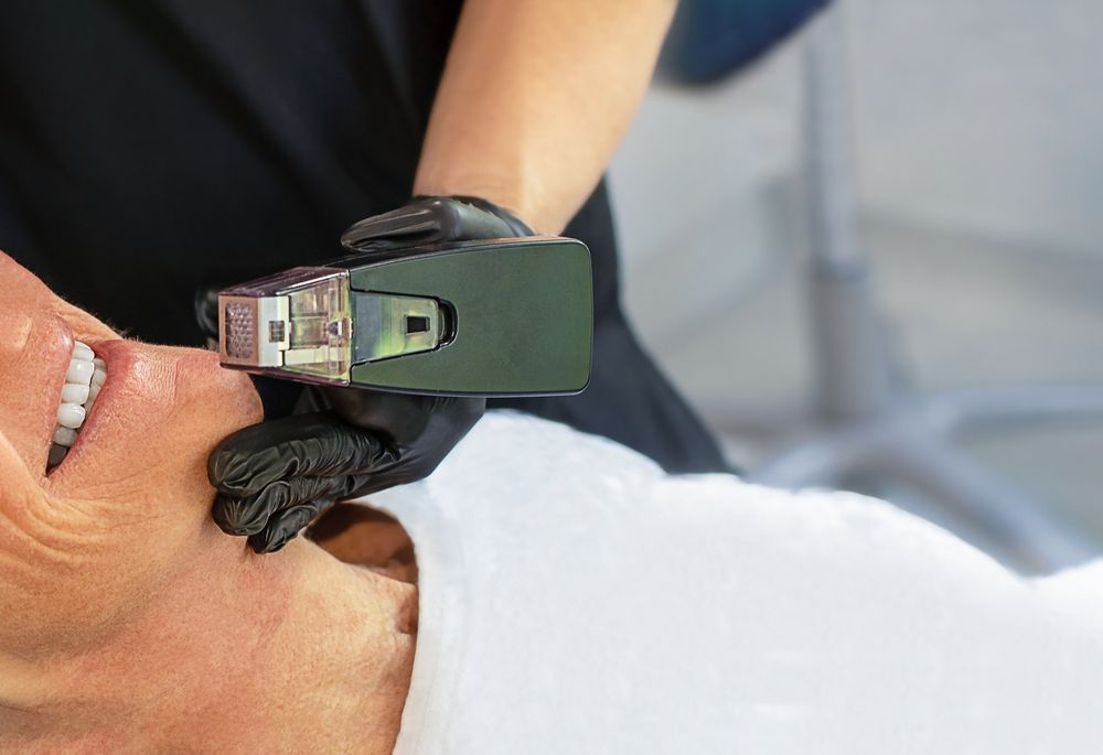 Person receiving cosmetic treatment to the face, held by gloved hands.
