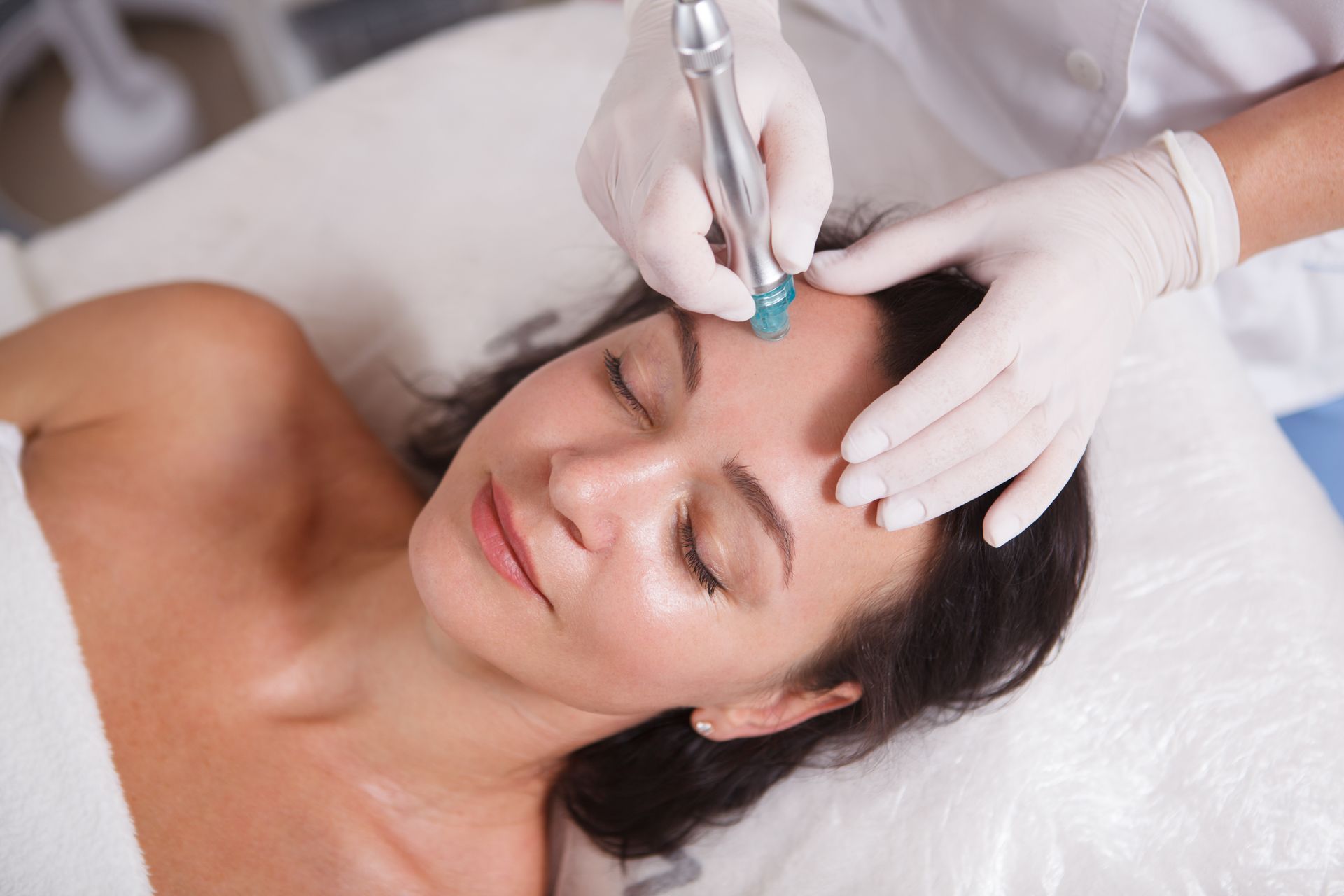 Woman receiving a facial treatment; device held to her forehead by gloved hand.