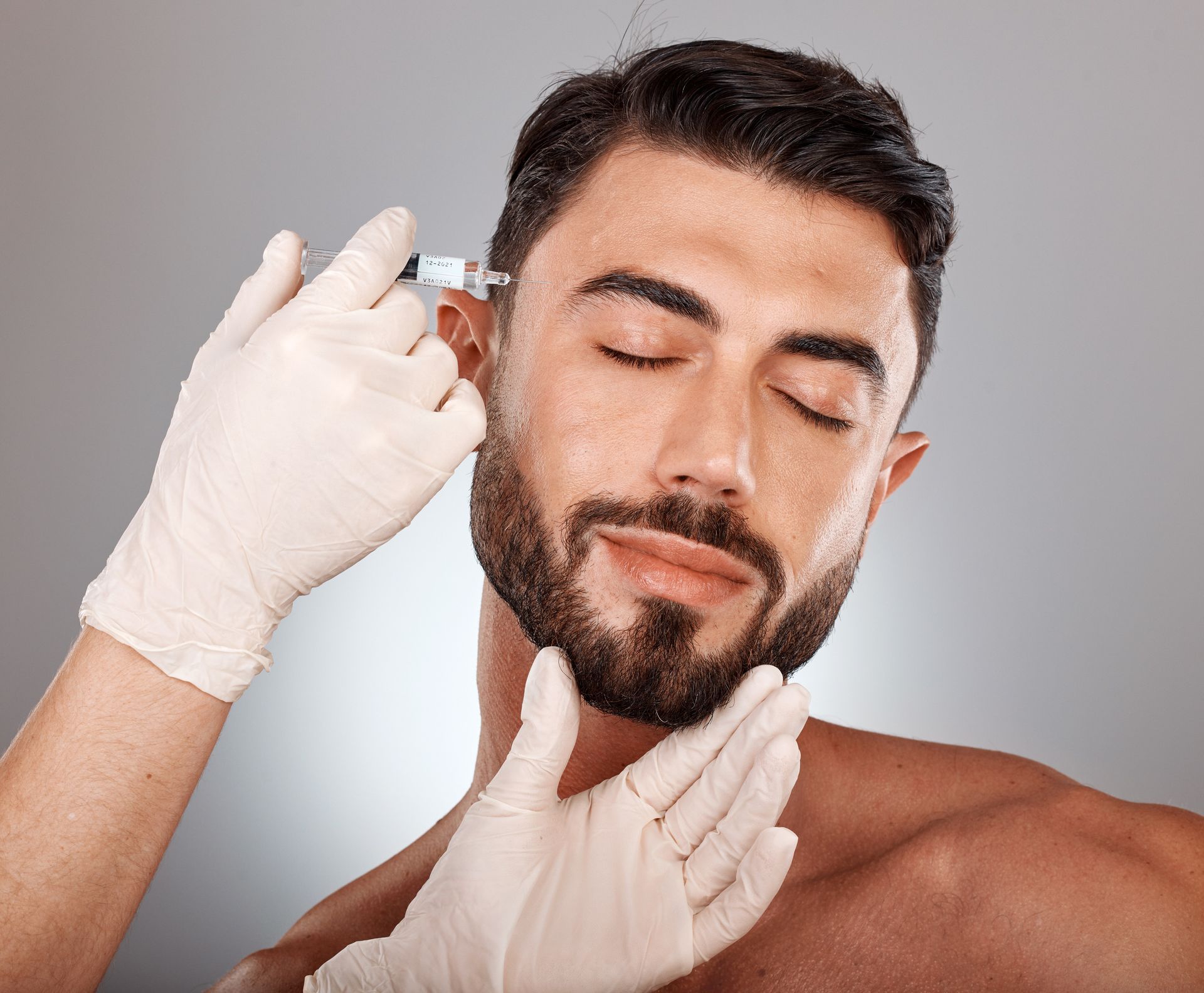 Man receiving injection near ear with eyes closed.
