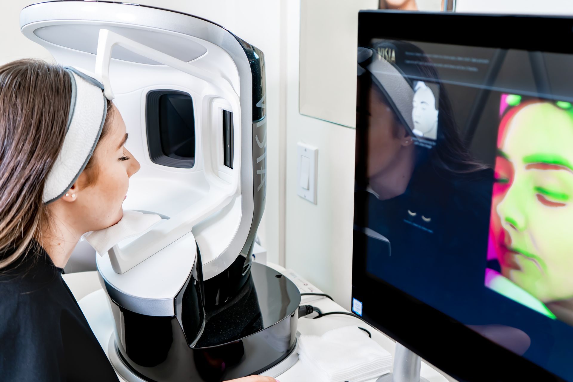 Woman having facial skin analysis using a device. Green and red facial mapping on screen.