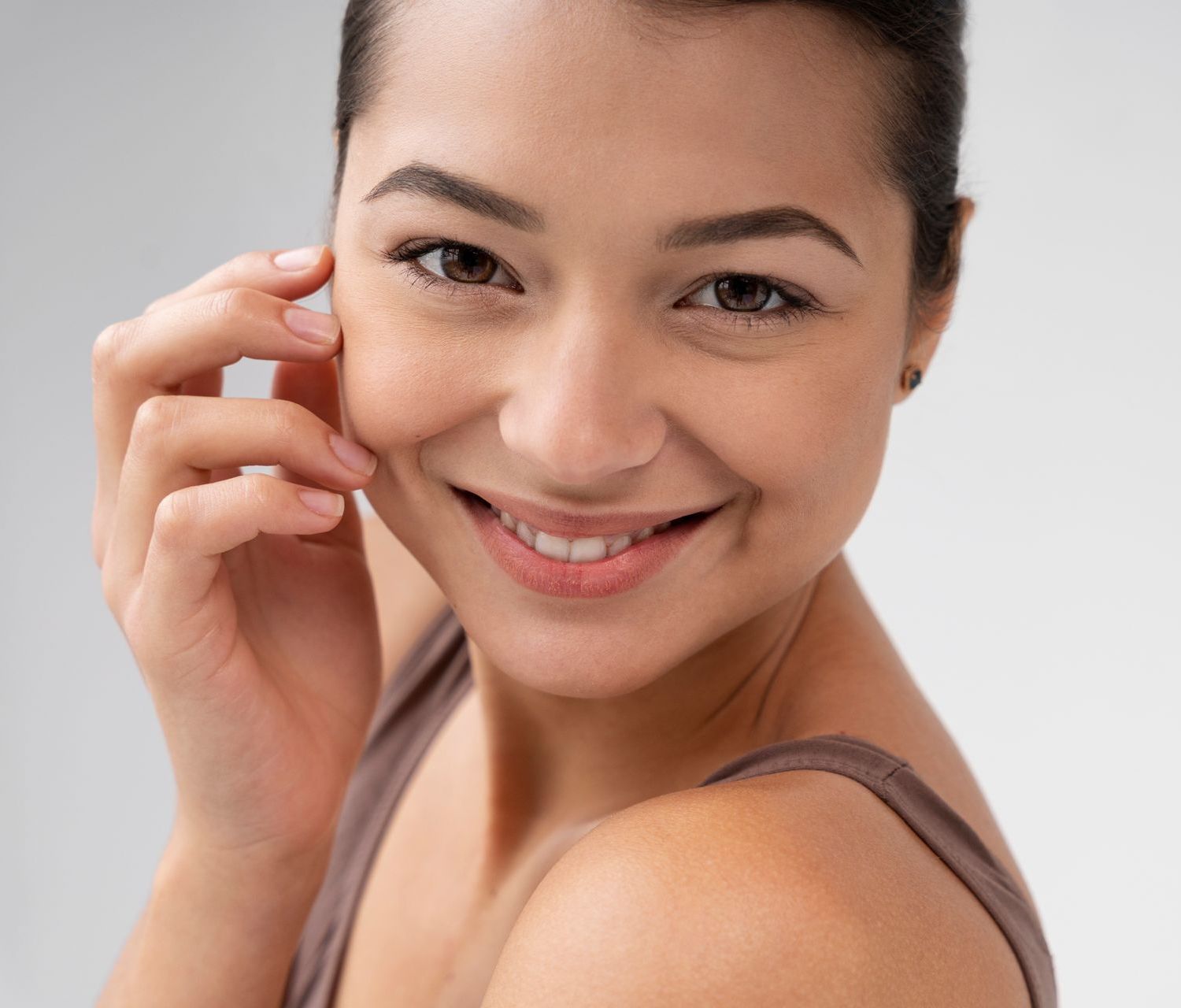 An elderly woman is smiling and touching her face with her hand.