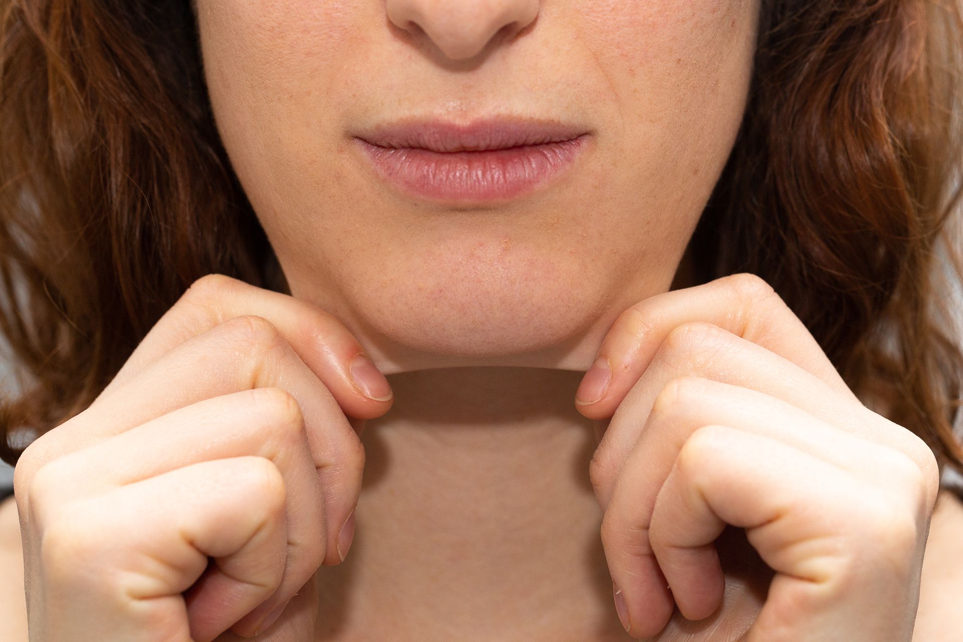 Woman holding skin under chin, examining for wrinkles.