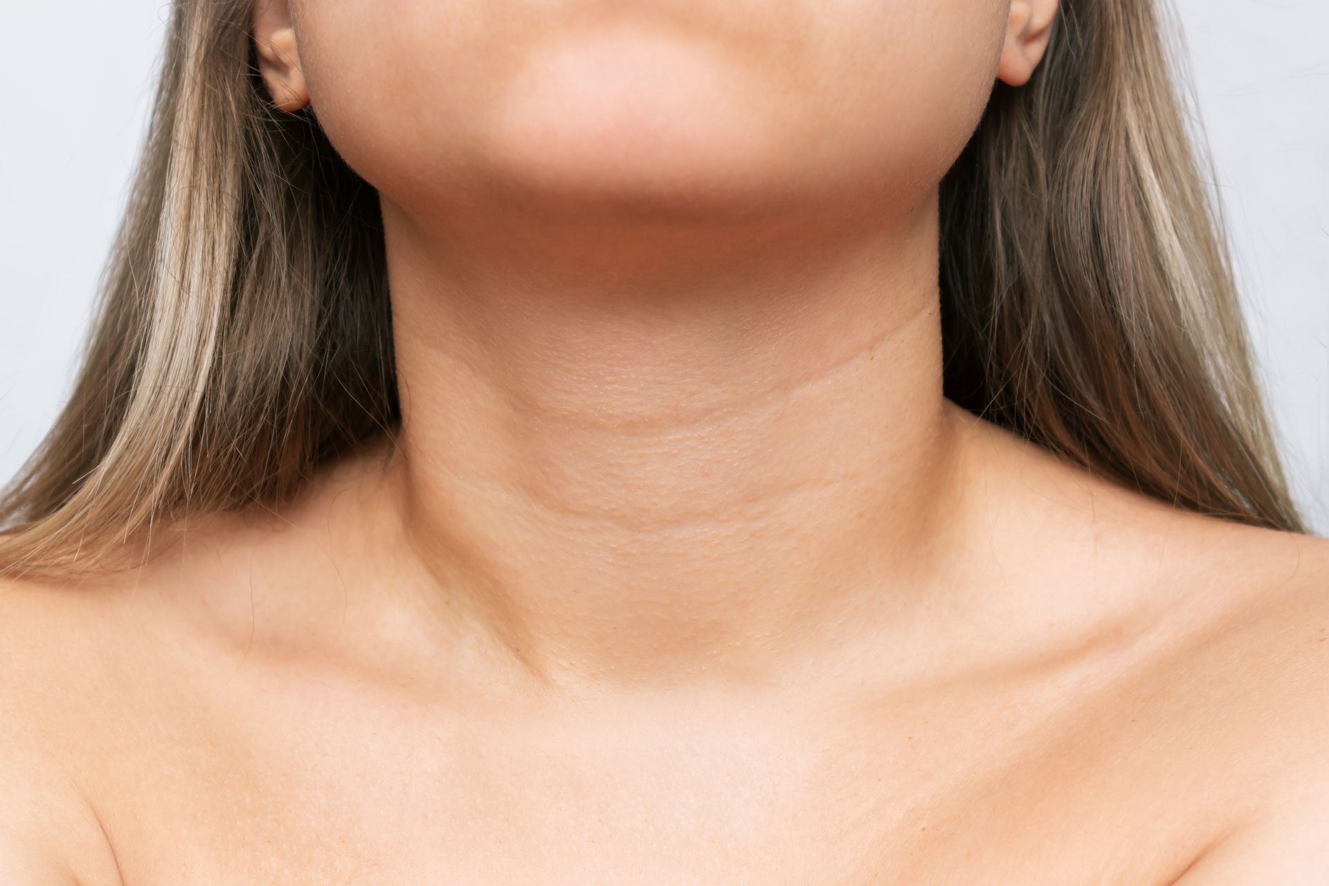Neck and upper chest of a person, showing skin with wrinkles, and collarbones, against a white background.