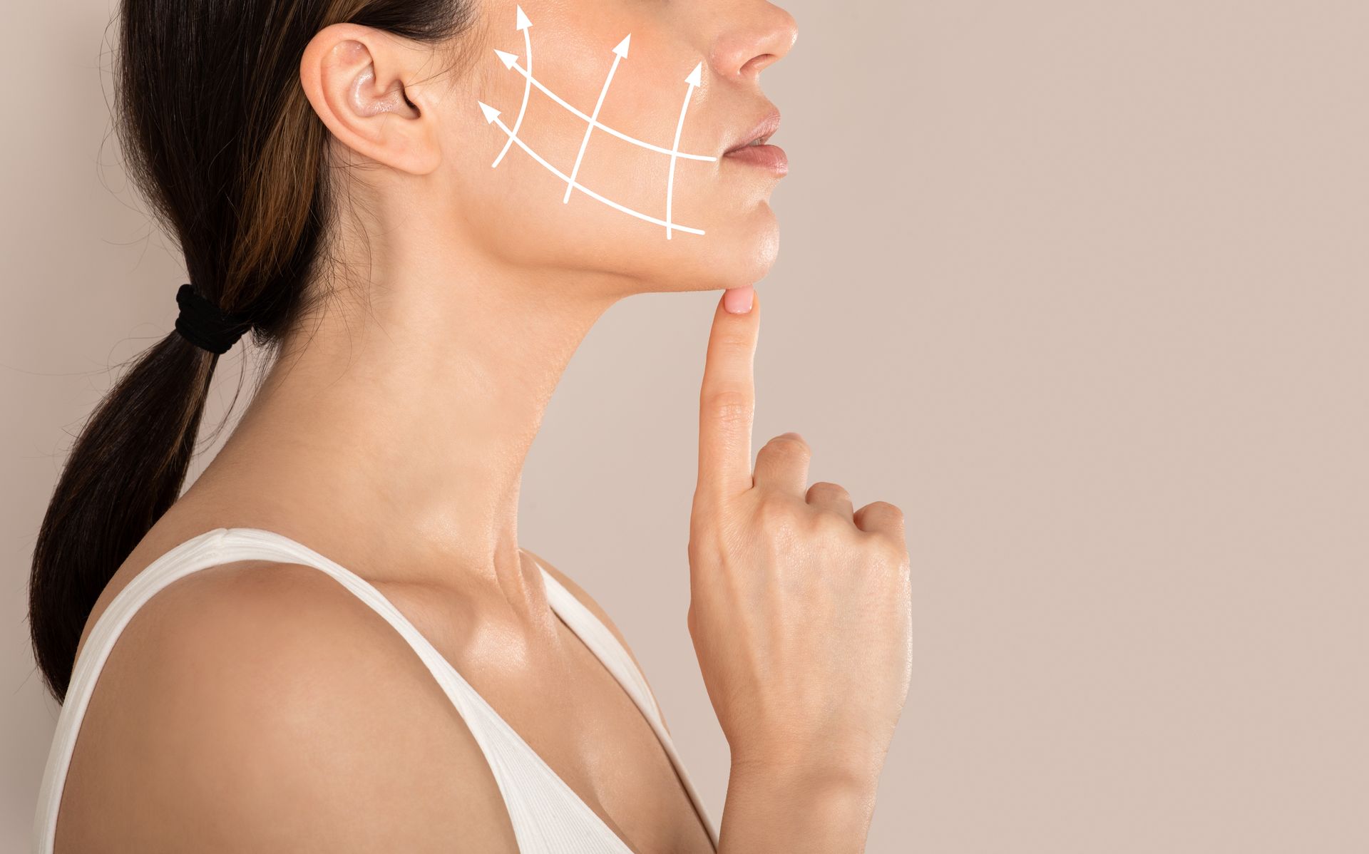 Woman's face with lift arrows, touching jaw. White tank top, beige background.