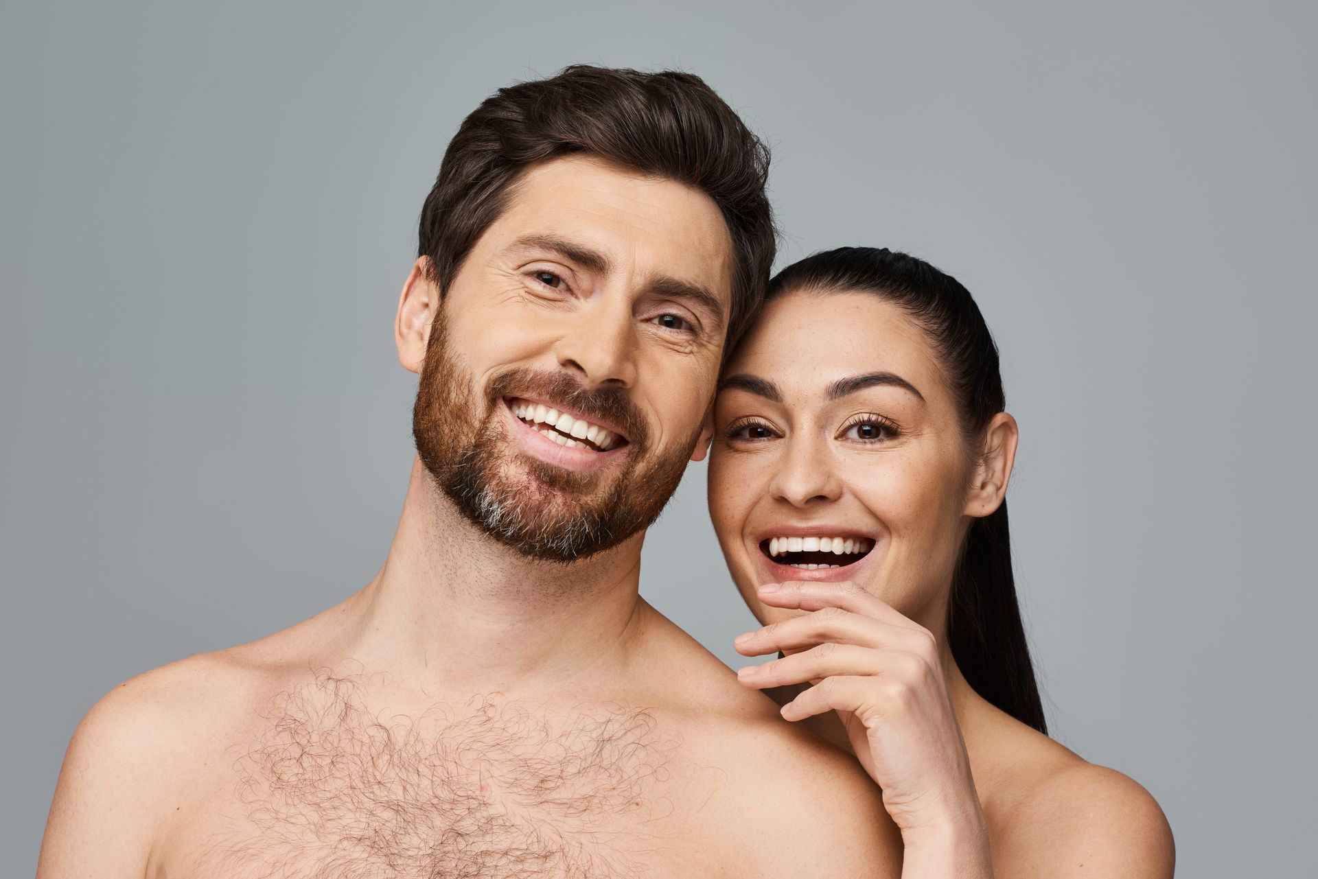 Man smiling, touching hair; bare chest, white background.