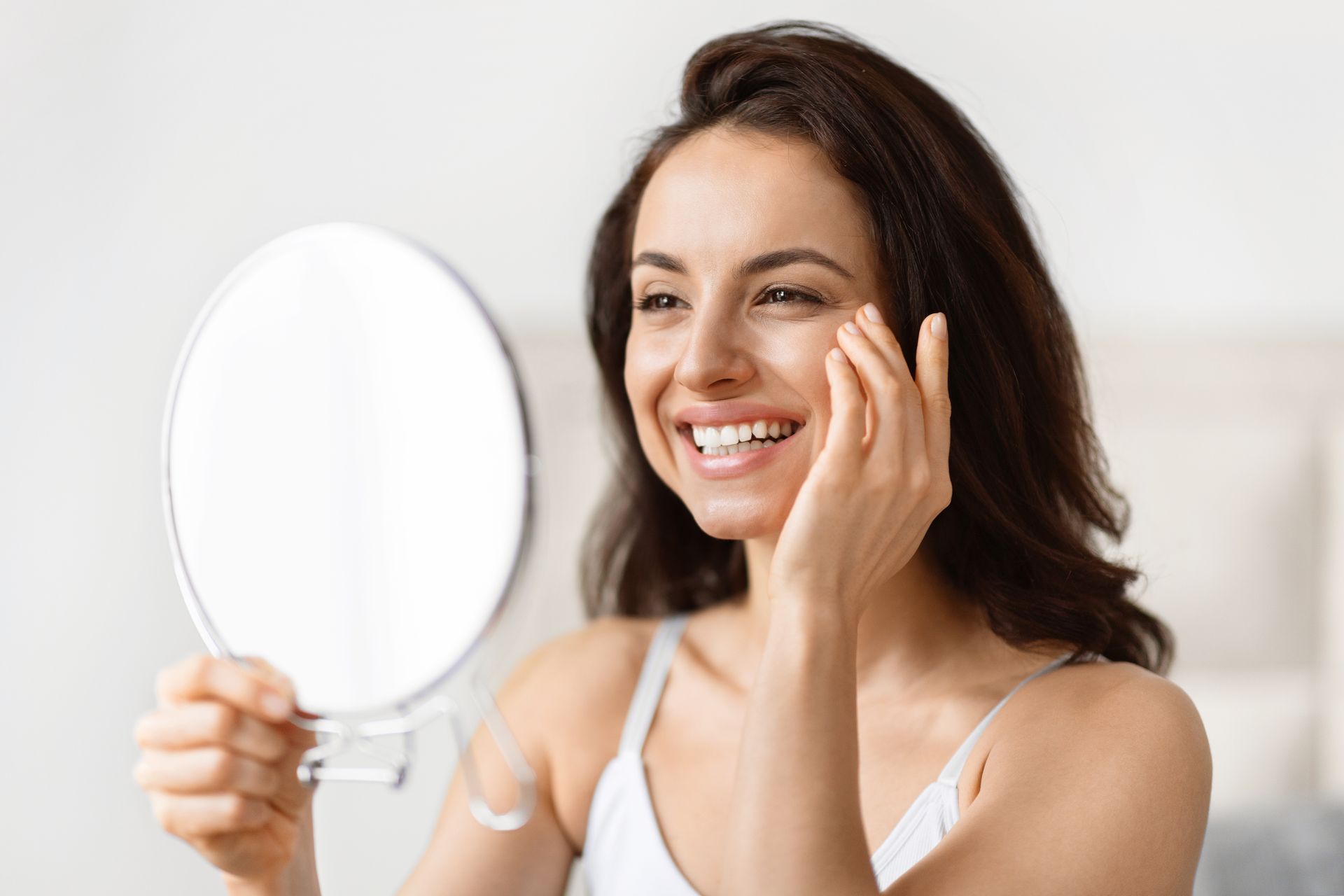 A woman is smiling while looking at her face in a mirror.