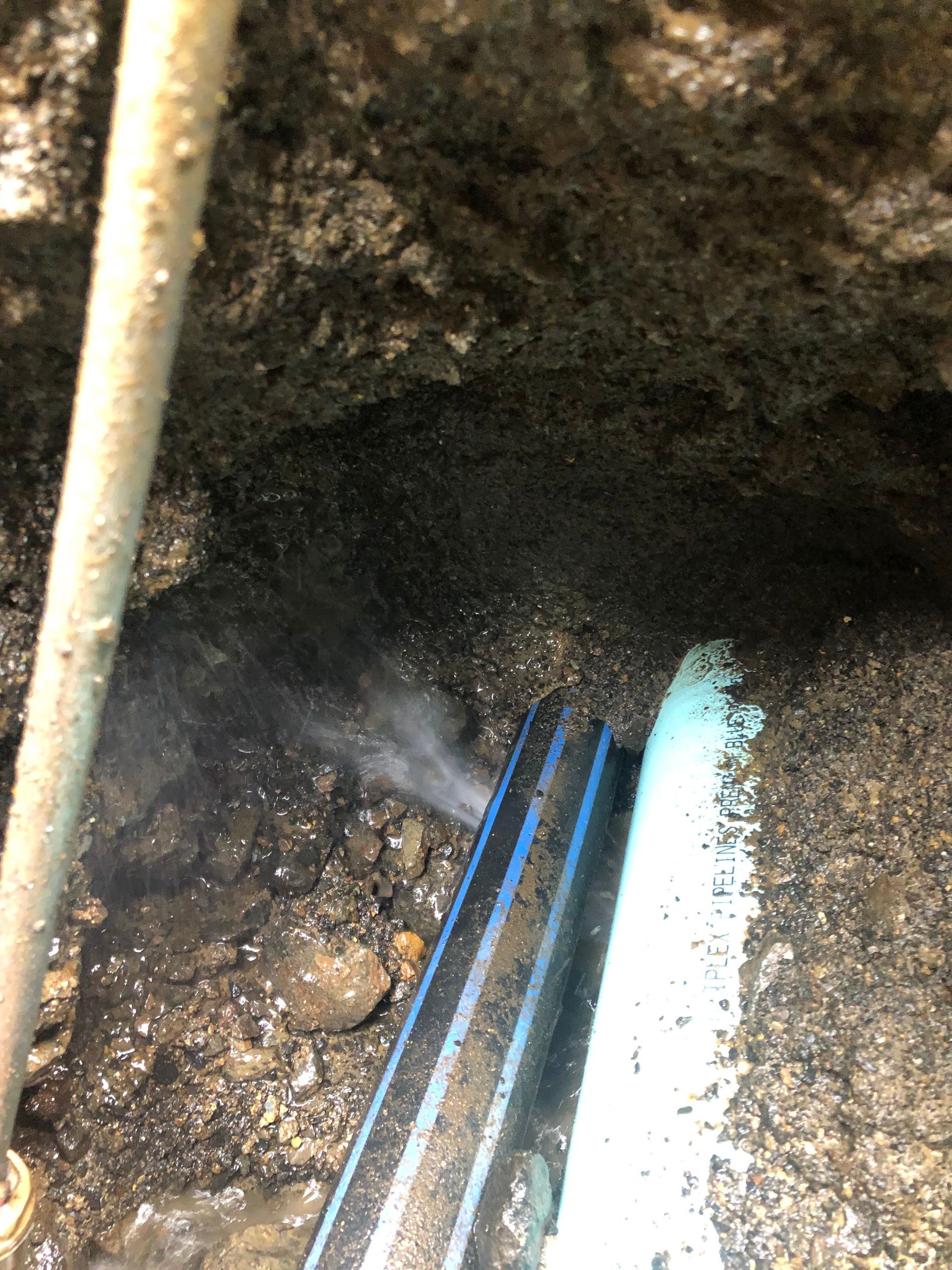 A blue pipe is laying in the dirt next to a white pipe.