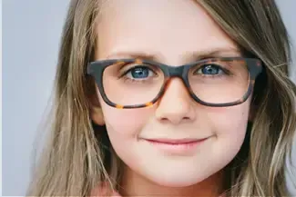 A young girl wearing glasses is smiling for the camera.