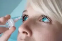 A woman is applying eye drops to her eye.
