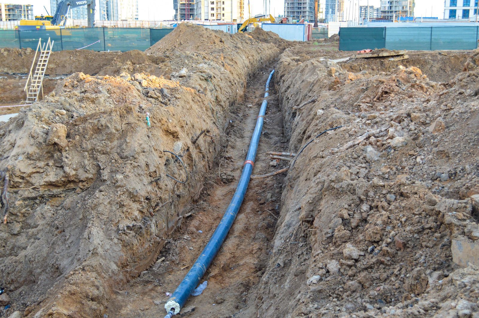A blue pipe is being installed in a trench at a construction site.