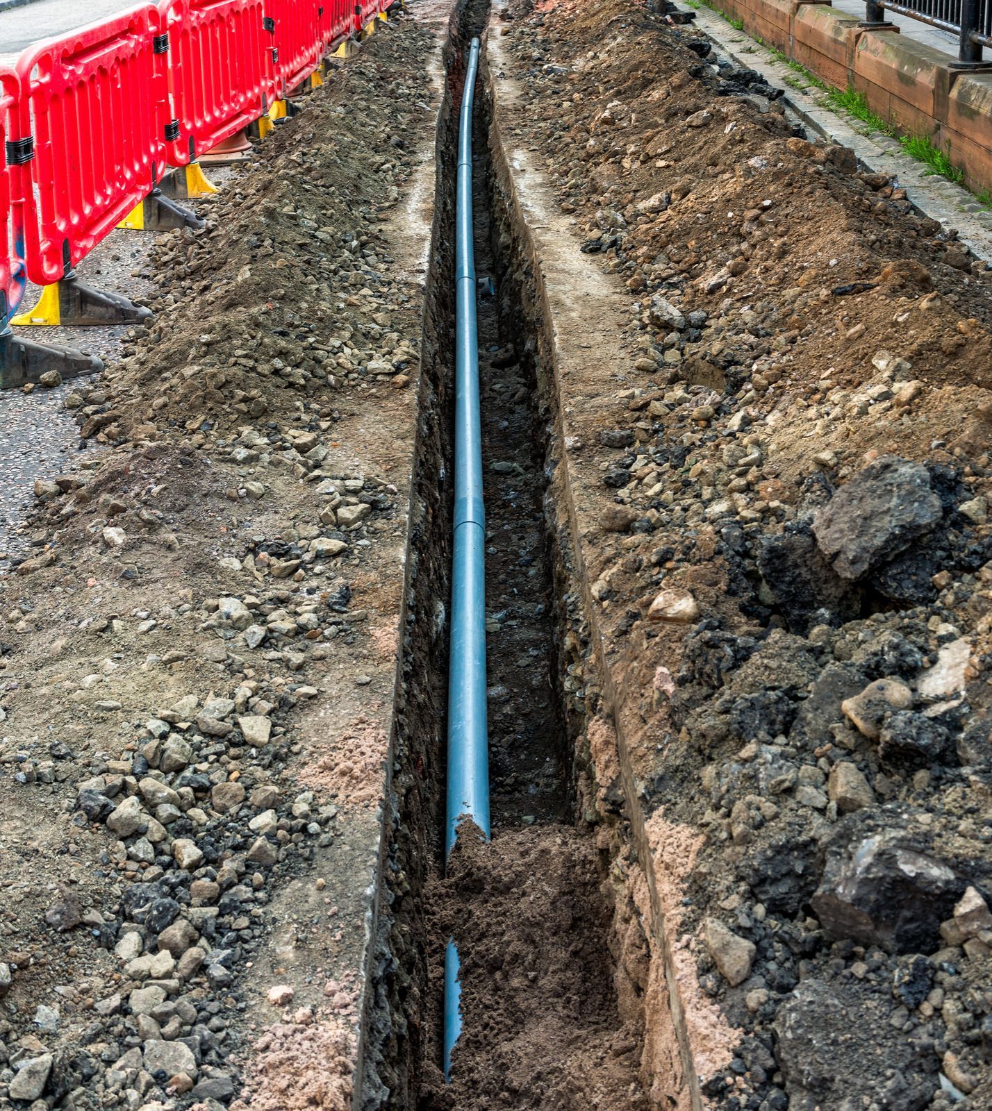 A blue pipe is being installed in a trench next to a road.