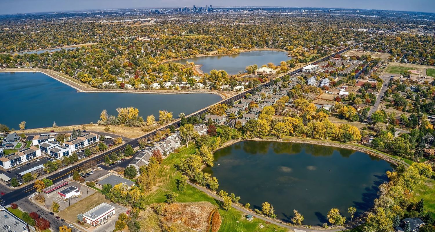 Aerial view of three lakes, connected by a road, surrounded by autumn trees and buildings, with a city in the distance.