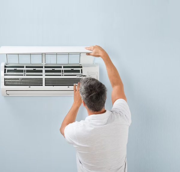 Person inspecting an air conditioner unit on a light blue wall.