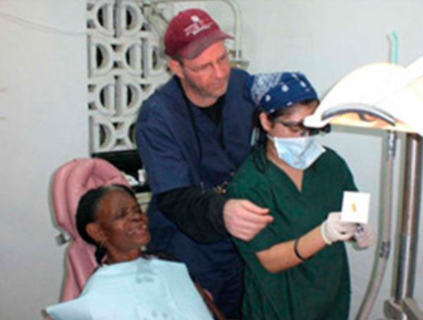 A man in a red hat stands next to a woman in a dental chair
