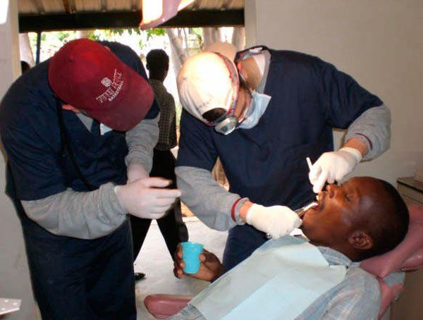 Two dentists are examining a patient 's teeth and one of them is wearing a red hat