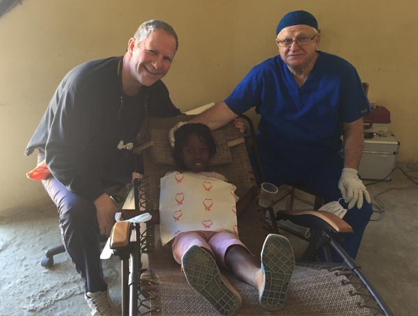 Two men are standing next to a little girl in a wheelchair