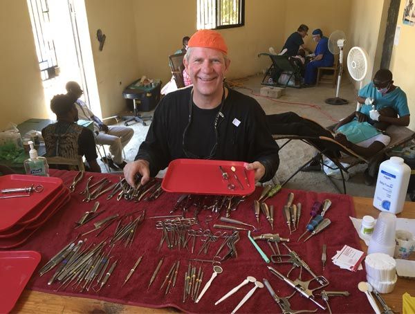 A man in an orange hat is holding a tray of dental instruments