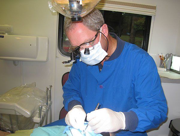 A dentist wearing a mask and glasses is working on a patient 's teeth