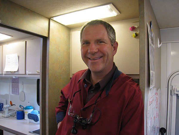 A dentist wearing a red coat and glasses is smiling