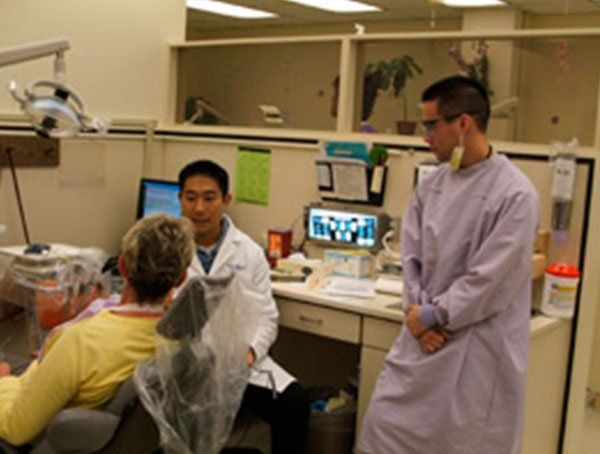 A man in a lab coat is standing next to a woman in a dental chair