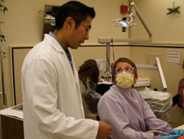 A man in a lab coat stands next to a woman in a dental chair