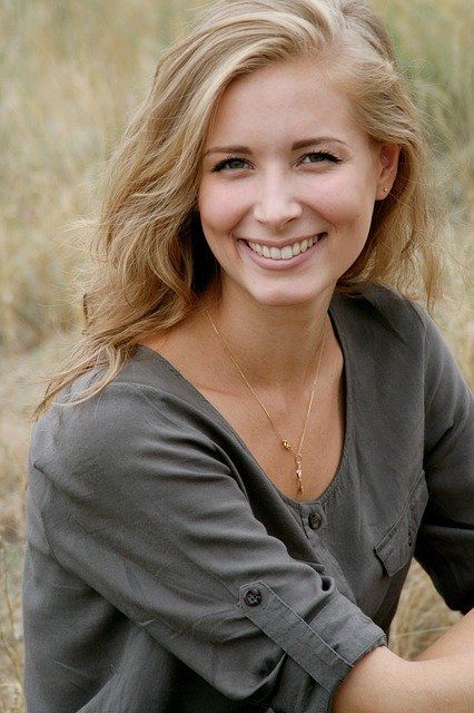 A woman is smiling while sitting in a field of tall grass.