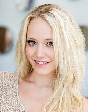 A woman with blonde hair and blue eyes is smiling for the camera.