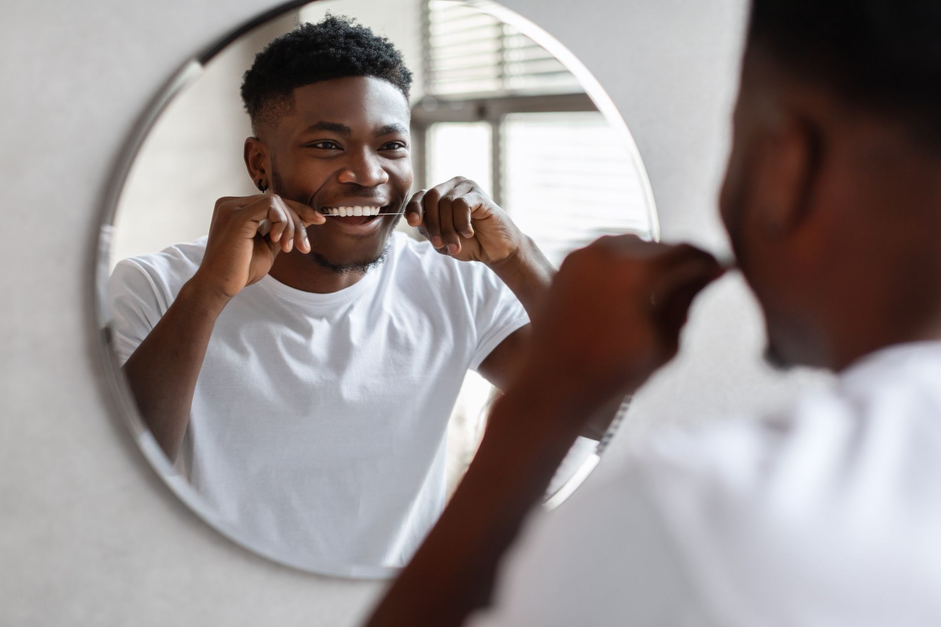 A man is flossing his teeth in front of a mirror.