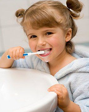 A little girl is brushing her teeth in a bathroom sink.