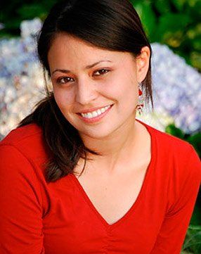 A woman wearing a red shirt and earrings is smiling for the camera.