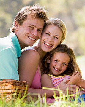 A family is sitting in the grass with a picnic basket.