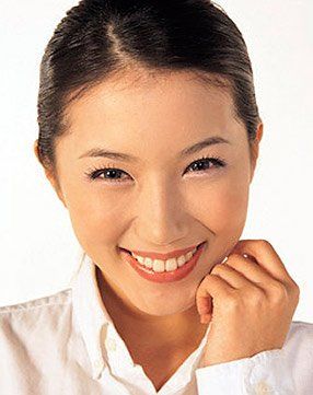 A woman in a white shirt is smiling with her hand on her chin.