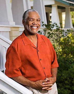 A man in an orange shirt is standing on the steps of a house.