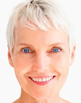 A close up of a woman 's face with short white hair and blue eyes smiling.