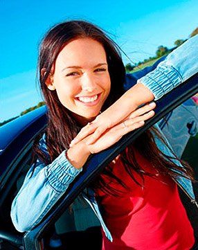 A woman is leaning out of a car window and smiling.