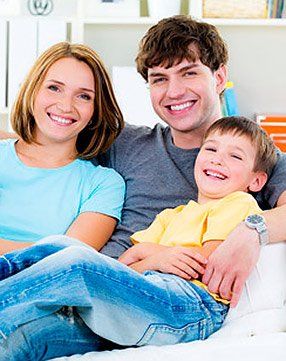 A family is sitting on a couch and smiling for the camera.