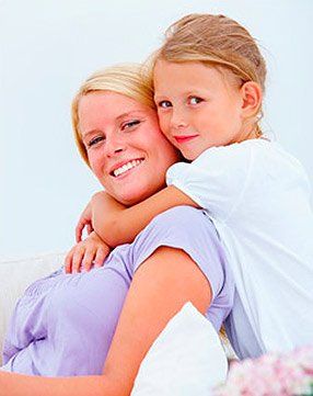 A little girl is hugging her mother on a couch.