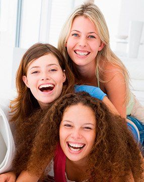 Three young women are laughing together while laying on a couch.