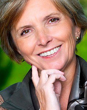 A close up of a woman smiling with her hand on her chin.