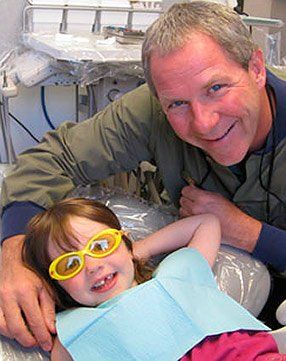 A little girl wearing sunglasses is sitting in a dental chair with a dentist.