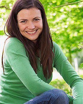 A woman in a green sweater is smiling while sitting under a tree.