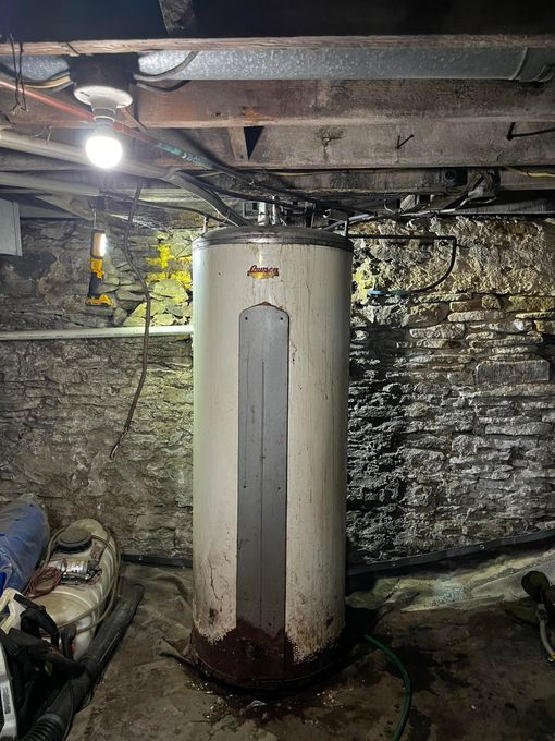 Water heater in a basement, surrounded by water and dark brick walls.
